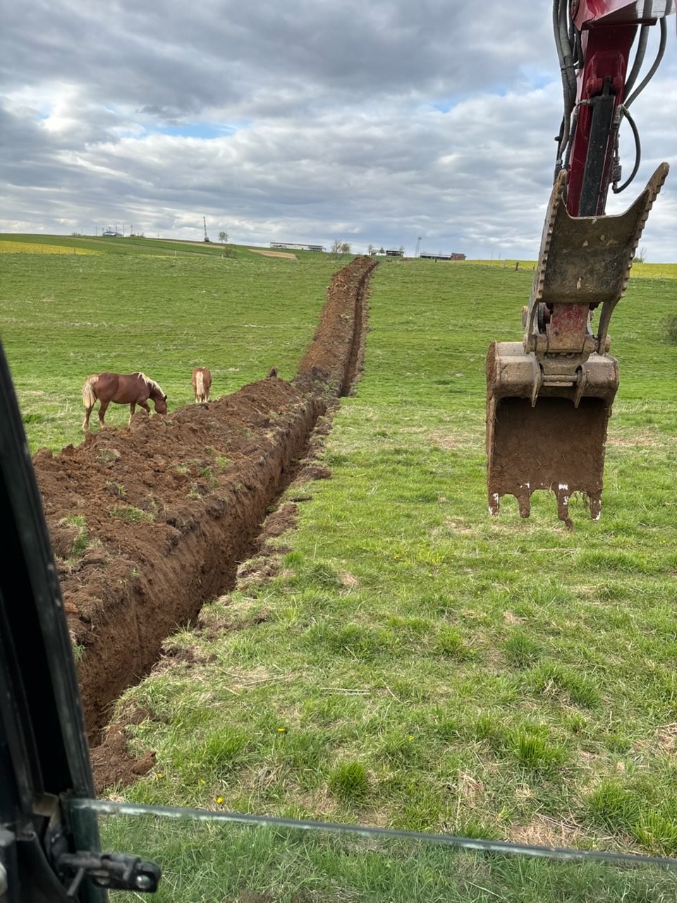 Excavator trenching through a pasture